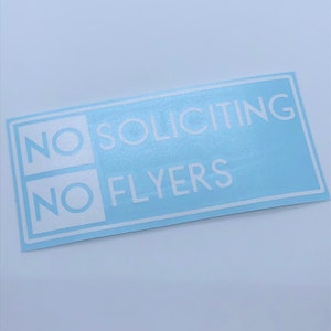 May include: A light blue sticker with white text that reads "NO SOLICITING NO FLYERS".