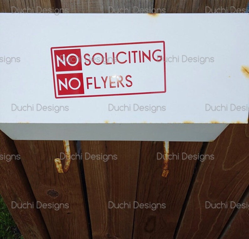 May include: White metal sign with red lettering that says "NO SOLICITING" and "NO FLYERS". The sign is mounted on a wooden fence.