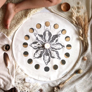 Könnte beinhalten: Ein weißer runder Wandteppich mit einem schwarzen und goldenen Mondphasen-Design. Das Design zeigt ein stilisiertes Bild einer Frau in jeder Mondphase. Der Wandteppich trägt den Text "art from the soul" in der rechten unteren Ecke.
