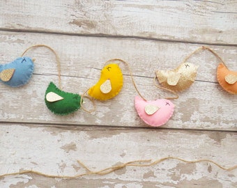 May include: A colourful felt garland with a string of birds in blue, green, yellow, pink, orange, and purple. Each bird has a gold glitter wing.