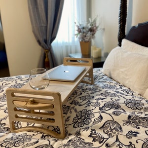 Large Adjustable lap desk set up on a bed to represent ability to work with a laptop from your bed. The desk is supporting a laptop and glass. We can clearly see the simple assembly mechanism with slots and dowel.