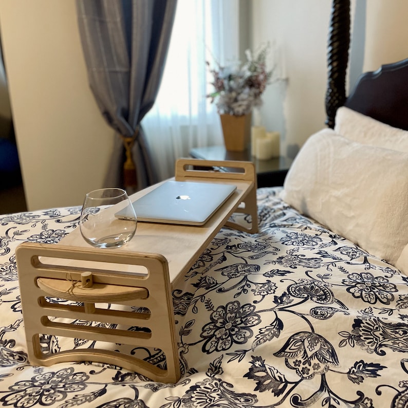 Large Adjustable lap desk set up on a bed to represent ability to work with a laptop from your bed. The desk is supporting a laptop and glass. We can clearly see the simple assembly mechanism with slots and dowel.