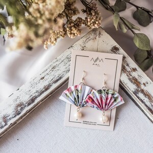 K&ouml;nnte beinhalten: Ein Paar Ohrringe mit floralem Muster aus Papierf&auml;cher mit Perlenakzenten. Die Ohrringe werden auf einer wei&szlig;en Karte mit dem Text "MM the Artist" und "Available Etsy shop.com/MMtheArtist London" pr&auml;sentiert.