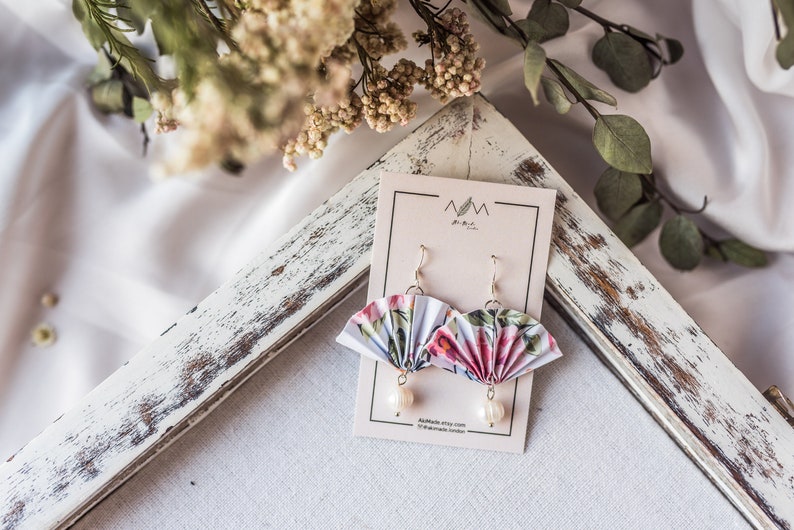 K&ouml;nnte beinhalten: Ein Paar Ohrringe mit floralem Muster aus Papierf&auml;cher mit Perlenakzenten. Die Ohrringe werden auf einer wei&szlig;en Karte mit dem Text "MM the Artist" und "Available Etsy shop.com/MMtheArtist London" pr&auml;sentiert.