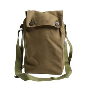 May include: A tan canvas messenger bag with a flap closure secured by two metal buttons. The bag has a long, olive green adjustable shoulder strap. The bag is made of a durable, textured fabric.