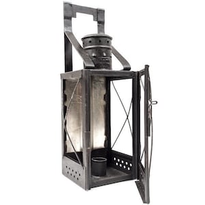 May include: A vintage black metal lantern with a rectangular body, a hinged door, and a handle. The lantern features a cylindrical top with air vents and a small cup inside. The open door reveals the interior, and the lantern is designed to be hung.