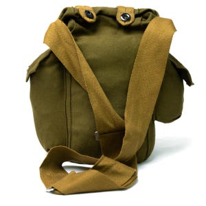 Puede incluir: Bolso de lona verde oliva con una correa para el hombro de color beige. El bolso tiene forma redondeada con dos cierres de botón en la parte superior. La correa es ajustable y se fija al bolso con herrajes metálicos.