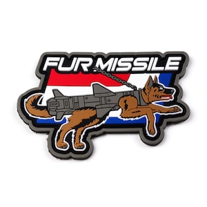 Pode incluir: Um patch retangular com as palavras "FUR MISSILE" em letras brancas sobre um fundo preto e vermelho. O patch apresenta um cão marrom com um míssil preso às suas costas, acorrentado ao redor do pescoço.