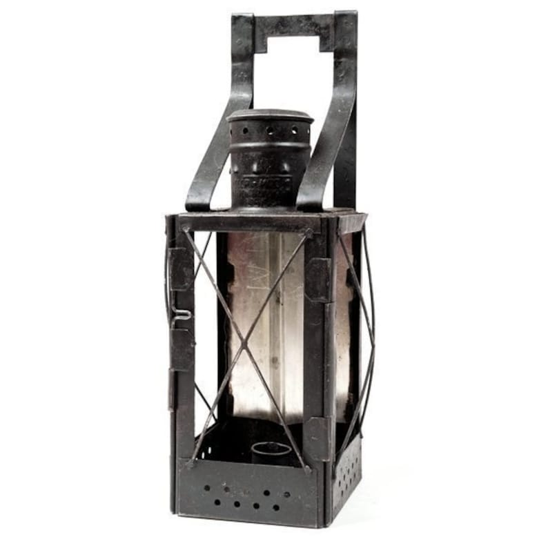 May include: A black metal lantern with a handle and glass panels. The lantern has a rectangular shape with a domed top and a series of small holes at the bottom. The handle is attached to the top of the lantern.