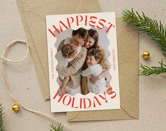 May include: Holiday greeting card with a family photo, the words "Happiest Holidays" in red, and the date "December 2024." The family is hugging each other. The card is on a kraft paper envelope.