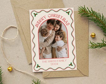 May include: Christmas card with a family photo inside a decorative frame. The card has a cream background with red and green accents, the words "MERRY CHRISTMAS" and "THE SMITH FAMILY 2024". The card is on a brown envelope.