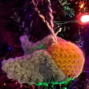 May include: A crocheted bird ornament with gray and yellow yarn, hanging on a Christmas tree with colorful lights.