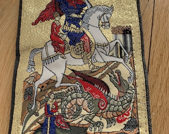 May include: A gold and black embroidered pouch with a depiction of Saint George slaying a dragon. The pouch has a zipper closure and the text "Θάιος Γεώργιος" is embroidered on the front.