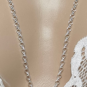 Op de afbeelding: Een zilveren ketting met een delicaat, rond schakeld ontwerp. De ketting wordt getoond op de nek van een mannequin.