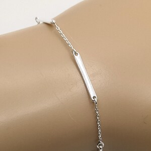 Peut inclure: Un bracelet en argent délicat avec une chaîne et trois accents rectangulaires. Le bracelet est présenté sur un poignet, soulignant son design minimaliste et sa surface réfléchissante. Le bijou est probablement en argent sterling.