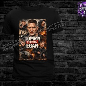May include: Black t-shirt featuring a graphic of a man with the text "Tommy Fucking Egan". The graphic includes images of the man in various poses. The shirt is displayed against a dark brick wall.