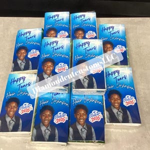 May include: A collection of party favours, each with a photo of a young man and the text "Happy Tears Heir Johnson Class of 2025". The favours are blue and white, with a purple design in the background.