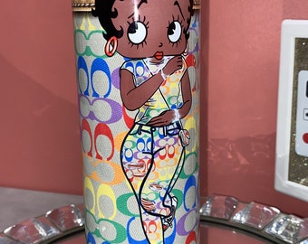 May include: A blue and white tumbler featuring a colourful cartoon image of a woman wearing a white shirt and blue jeans. The background is a colourful pattern of the letter "C".