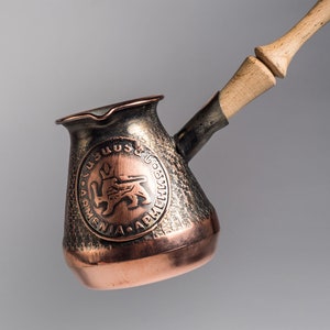 May include: A copper and brass coffee pot with a wooden handle. The pot has an embossed design with the words "ՀԱՅԱՍՏԱՆ" and a lion emblem.