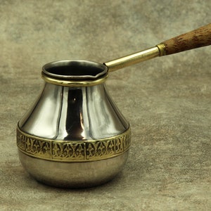 Może przedstawiać: Turkiecki czajnik do kawy ze srebra i mosiądzu z drewnianym uchwytem. Czajnik ma ozdobny pasek wokół środka.