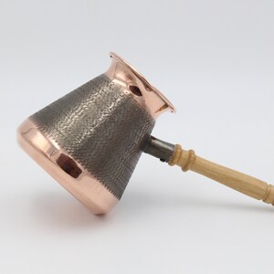 May include: A copper coffee pot with a hammered finish and a wooden handle. The pot is designed for brewing Turkish coffee.