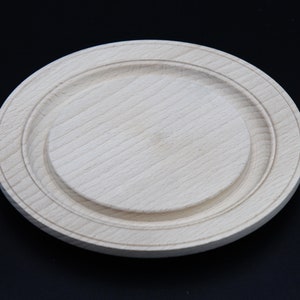 May include: A round wooden plate with a raised edge and a smooth, light wood finish.