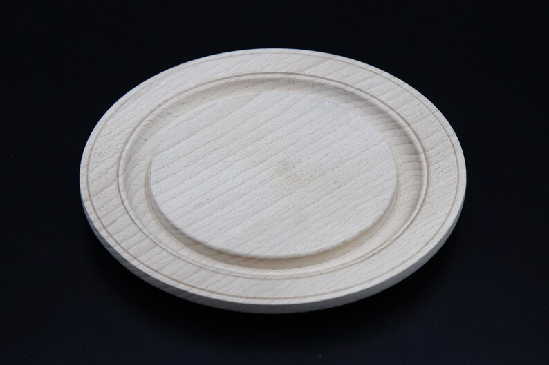 May include: A round wooden plate with a raised edge and a smooth, light wood finish.