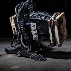 May include: A black sculpture of a creature with mechanical elements, including computer fans with tan and brown details, and a network of tubes and wires. The sculpture is positioned on a dark surface.