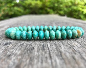 May include: A beaded bracelet composed of numerous round, turquoise-coloured stones. Each bead features a smooth, polished surface with natural variations in colour, including shades of teal, light blue, and occasional tan or brown inclusions.