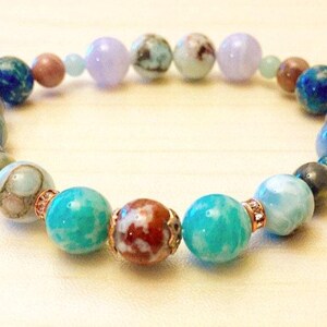 May include: A beaded bracelet featuring a variety of colorful gemstone beads. The bracelet includes turquoise, blue, brown, and lavender beads. The beads are strung together with a gold-colored metal. The bracelet is a piece of jewelry.
