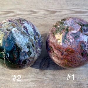 May include: Two polished green, purple, and white jasper spheres. The spheres are about the same size and have a swirling pattern. The sphere on the left is labelled #2 and the sphere on the right is labelled #1.