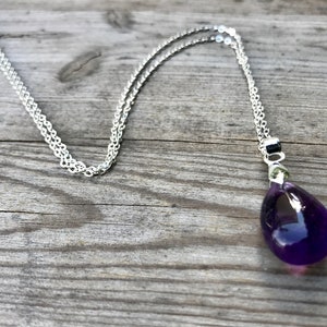 May include: A silver chain necklace with a teardrop-shaped amethyst pendant.