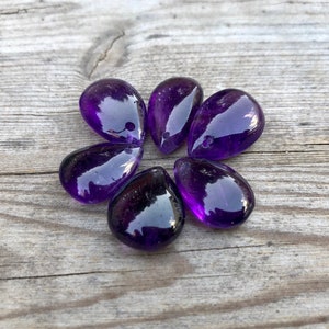 May include: Six teardrop-shaped amethyst gemstone beads with a hole drilled through the top for stringing.