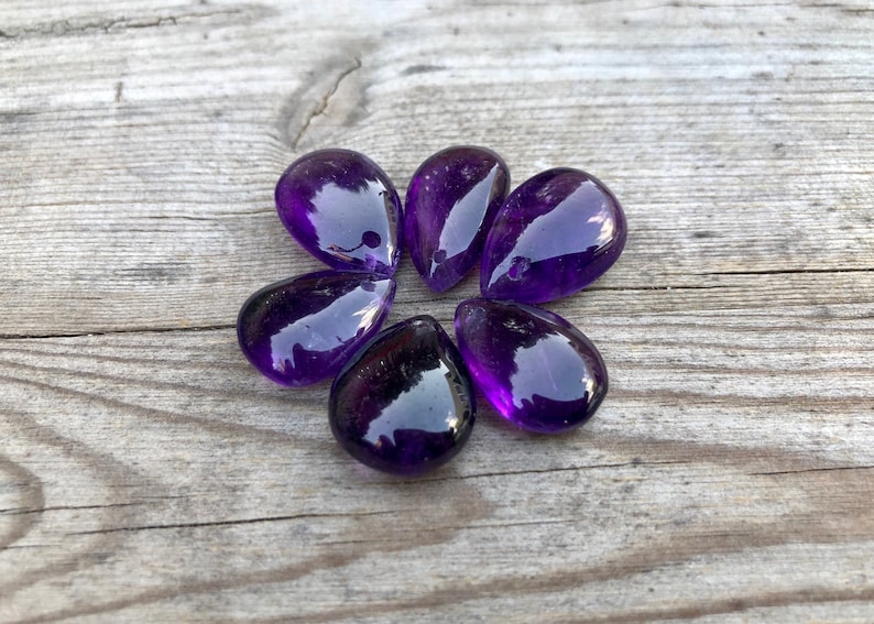 May include: Six teardrop-shaped amethyst gemstone beads with a hole drilled through the top for stringing.