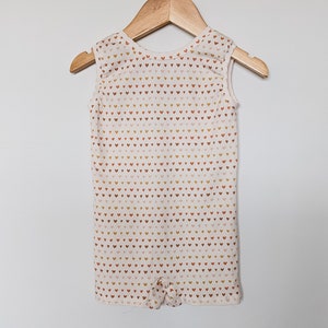 May include: A sleeveless white onesie with a pattern of small brown, orange, and pink hearts.