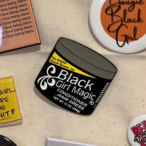 May include: A collection of pins and magnets with empowering messages. The central item is a black jar labeled "Black Girl Magic" with a net weight of 12 oz. Other items include pins with phrases like "Bougie Black Girl" and "Hey Black Girl, You're the Shit."