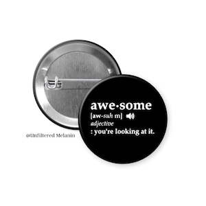 May include: A black button pin with the word "awesome" in white, along with its pronunciation and definition. The pin is round and has a metal back. The text "you're looking at it" is also included.