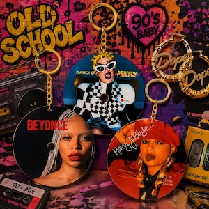 May include: Three circular keychains featuring portraits of musical artists. One shows Beyonce, one shows Cardi B with the text Privacy, and one shows Mary J. Blige with the text I'm Goin' Down. Each keychain has a gold metal ring and chain.