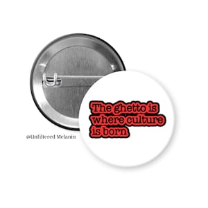 May include: A white button with the text "The ghetto is where culture is born" in red lettering. The back of the button is silver with a safety pin clasp.