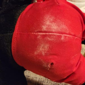 May include: A red plush toy with black fur and a white patch. The toy has a small hole in the red fabric.