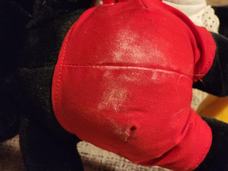 May include: A red plush toy with black fur and a white patch. The toy has a small hole in the red fabric.