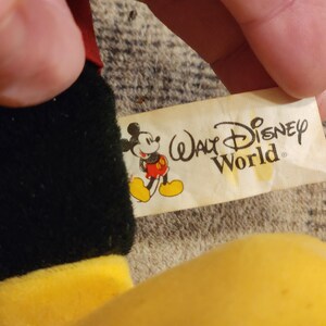 May include: A black and yellow plush Mickey Mouse toy with a white tag that reads "Walt Disney World".