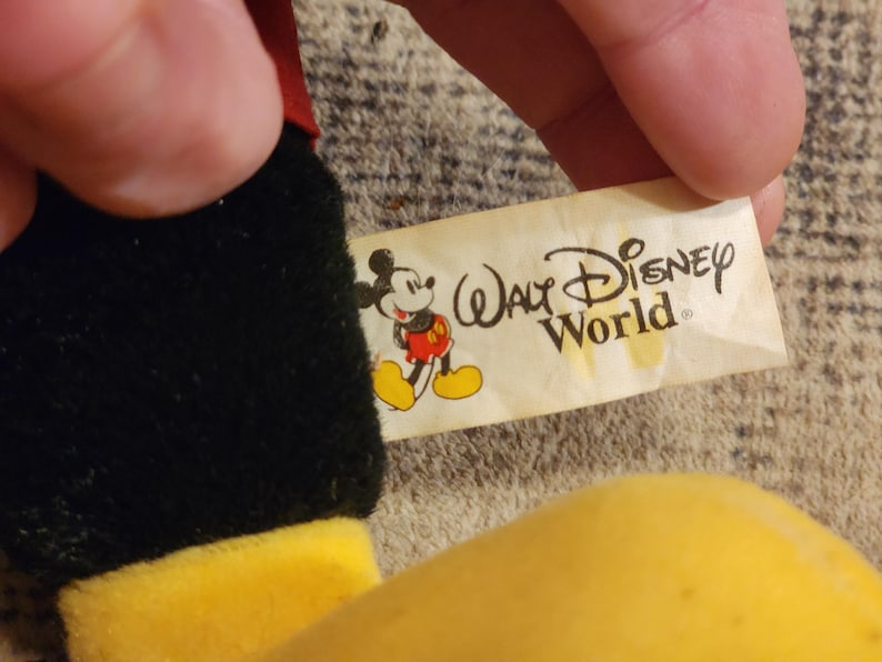 May include: A black and yellow plush Mickey Mouse toy with a white tag that reads "Walt Disney World".