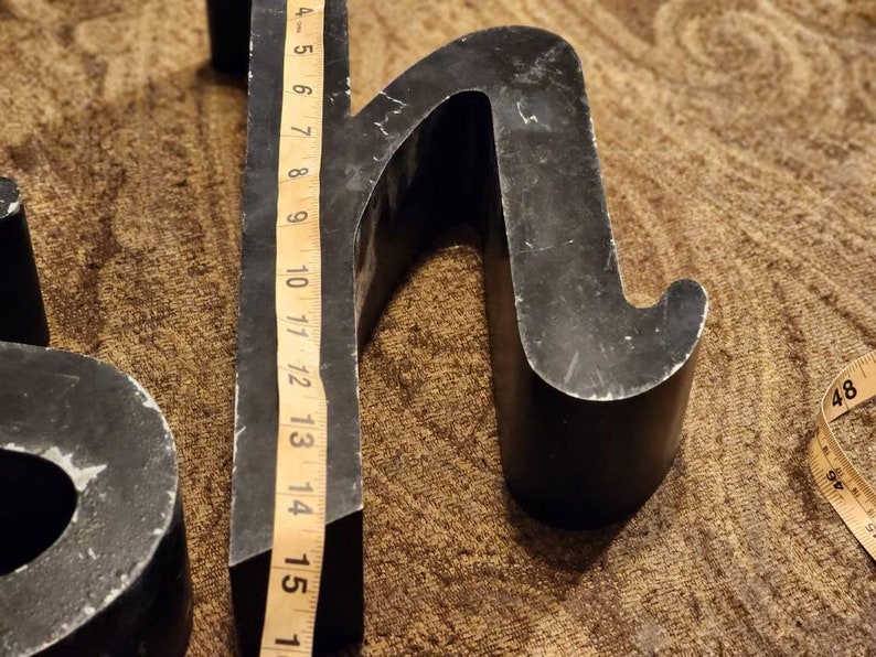 Puede incluir: Letras de metal negro, la letra "H" tiene 15 pulgadas de alto, la letra "S" tiene 10 pulgadas de alto. Las letras est&aacute;n sobre una alfombra marr&oacute;n.