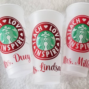 May include: Three white plastic cups with red and green designs. The cups have the text "Teach Love Inspire" and a green Starbucks logo. The cups are personalized with the names "Mrs. Duey", "Mrs. Lindsay", and "Mrs. Miller".