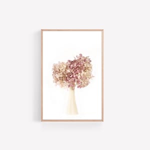 May include: A bouquet of dried hydrangeas in shades of pink and white arranged in a white ceramic vase. The flowers are against a white background.