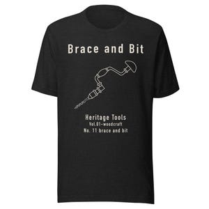 May include: Dark grey t-shirt featuring the text "Brace and Bit" above a white line drawing of a brace and bit tool. The text "Heritage Tools Vol.01-woodcraft No. 11 brace and bit" is below the tool.