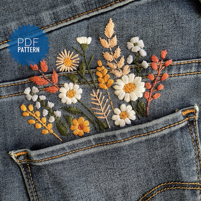 Wildflower embroidery PDF pattern for jeans pocket. Hand-stitched floral bouquet featuring white daisies, yellow flowers, and autumn-colored leaves on blue denim. Digital download guide for DIY clothing upcycling.