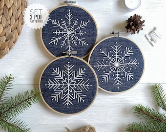 May include: Set of three embroidery hoop patterns featuring white snowflake designs on a dark blue denim background. The text "SET 3 PDF PATTERNS" is printed on a white star.
