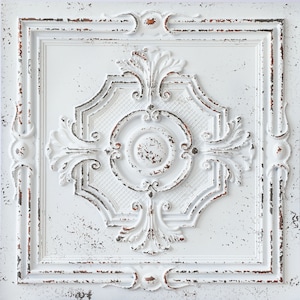 Op de afbeelding: Witte plafondtegel met een verweerde, antieke uitstraling. De tegel heeft een reliëf, versierd ontwerp met een centrale cirkel en ingewikkelde bloemmotieven.